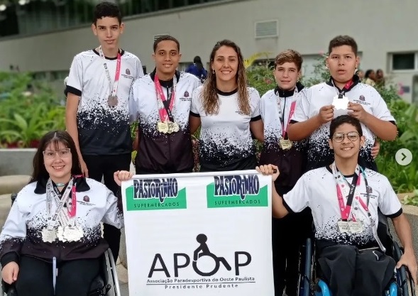 Atletas e treinadora com medalhas e banner da equipe nas Paralimpíadas Escolares
